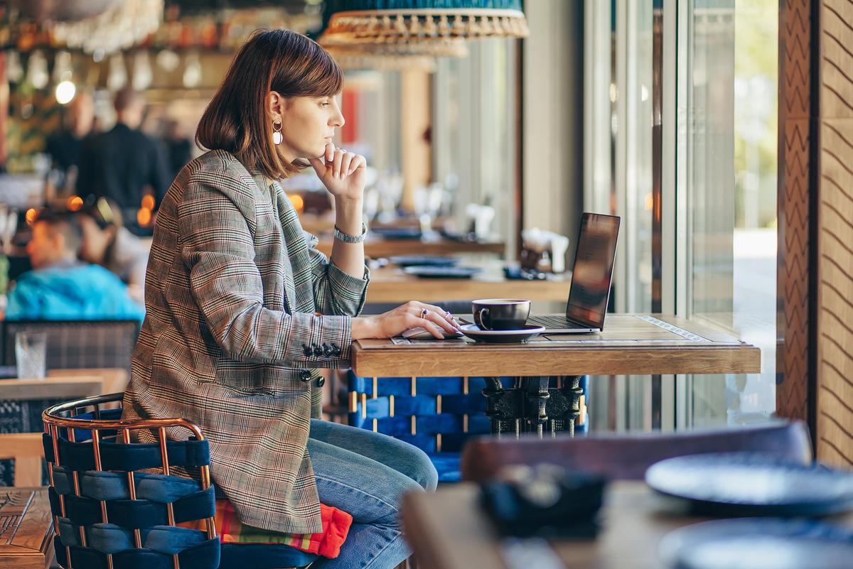 Porträt einer jungen Freiberuflerin, die in einem Café sitzt und einen Laptop für eine Fernarbeit benutzt.